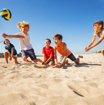 Groepje kinderen spelen volleybal op het strand, jongen slaat op